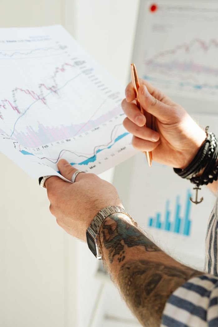 About Close-up of a person's hands holding financial charts and graphs with a pen.