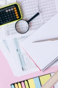 Home-test Flat lay of financial documents, calculator, magnifying glass, and notebook on a pastel background.
